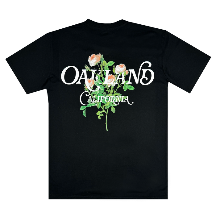 The Posy Tee from Oaklandish, part of the men's collection, is a black cotton T-shirt adorned with white stylized text displaying "OAKLAND" above the smaller "CALIFORNIA." The design is beautifully enhanced by an illustration of pink roses with green leaves, elegantly centered on the back.