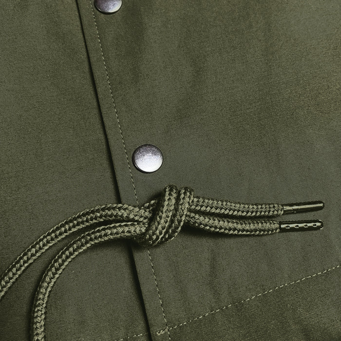 Close-up of a khaki green fabric with a drawstring featuring two black aglets tied in a knot. The fabric is part of the Premium Coaches Jacket by Oaklandish, showcasing visible stitching details and silver snap buttons. The texture and weave of this water-resistant outerwear material are clearly visible in the image.