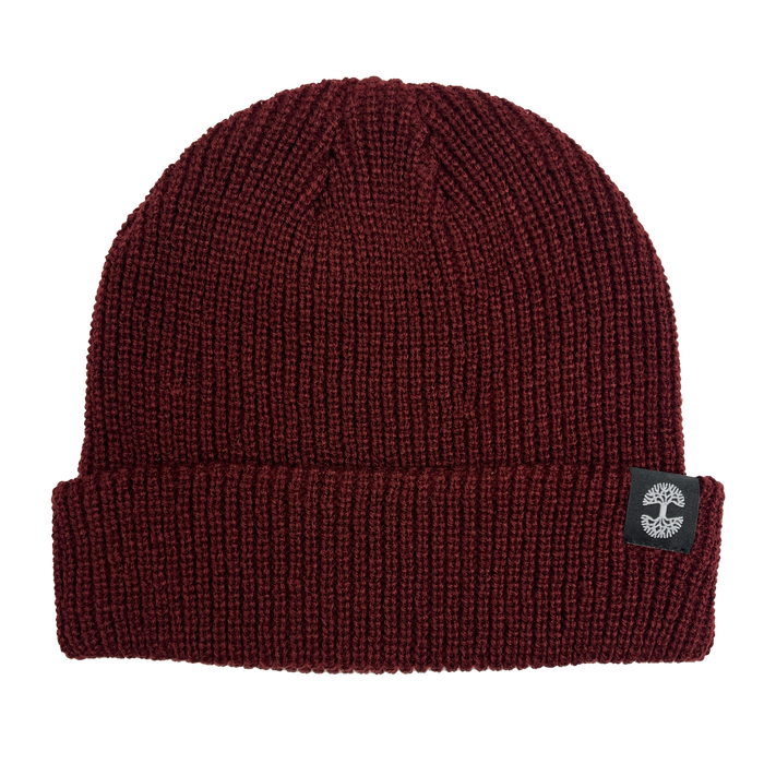 The Ramos Beanie by Oaklandish is a maroon acrylic headwear featuring a ribbed texture and folded brim. It includes a black fabric tag on the brim adorned with a white circular logo, providing cozy style and warmth for cold weather.