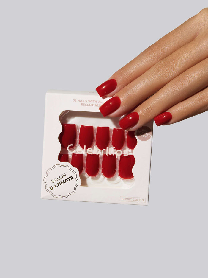 Hand with bright red coffin press-on nails holding a box of the nails.