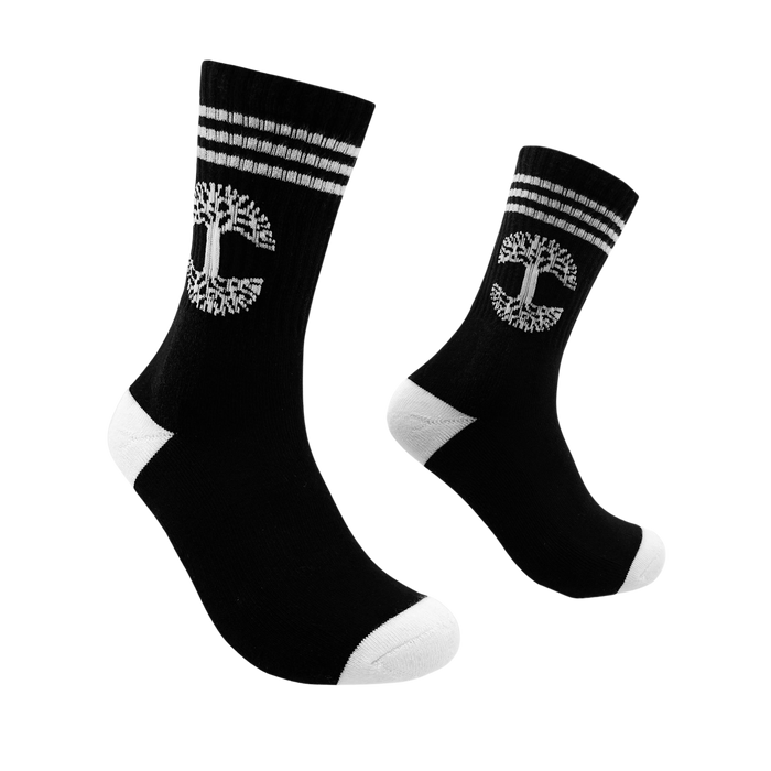 A pair of Retro Classic Socks by Oaklandish, designed in black with three white stripes at the top and a distinctive tree-like Oaklandish logo encased in a circular border. The toes and heels, also white, provide a striking contrast. These exceptionally comfy mid-calf socks are displayed side by side, angled slightly with toes pointing upward against a plain white background.