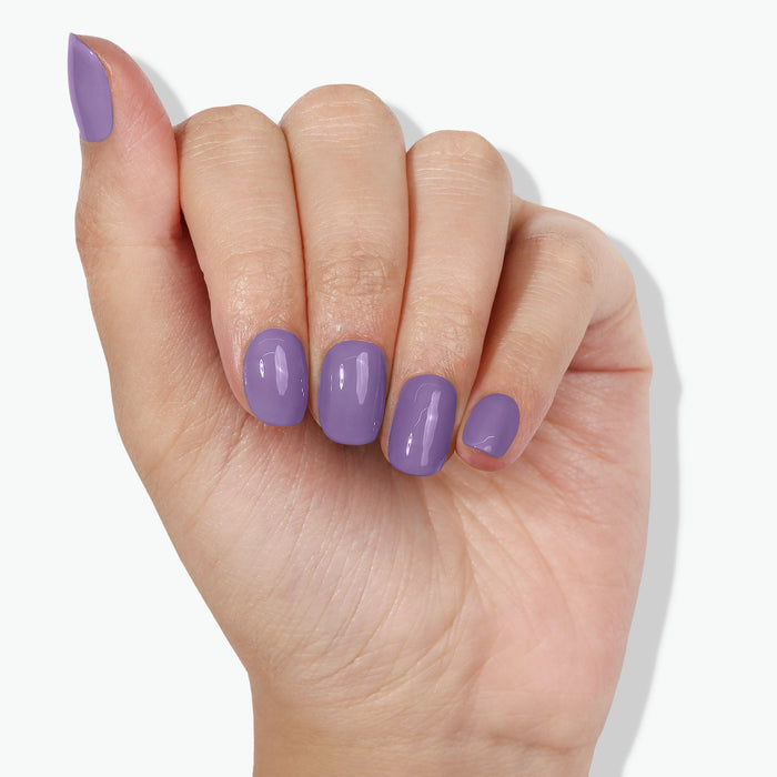 A hand with a Road Trip manicure by LONDONTOWN, featuring a psychedelic lavender design, is shown against a plain background. The nails are medium length and neatly shaped.