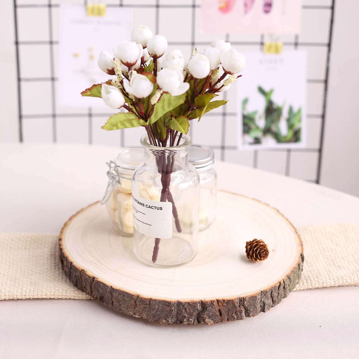 Artificial cotton flower arrangement in glass vase on wooden slice.