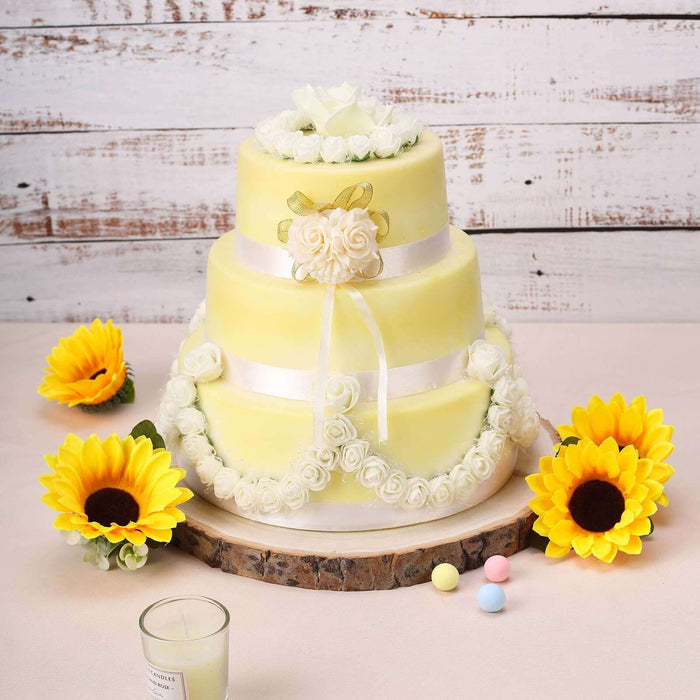 Yellow wedding cake with floral decorations and sunflowers on a rustic wooden table.