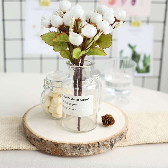 White floral arrangement in a glass jar on a wooden slice.