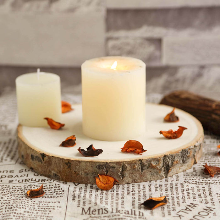 Candles on a wooden slice with dried petals, set against a textured background.