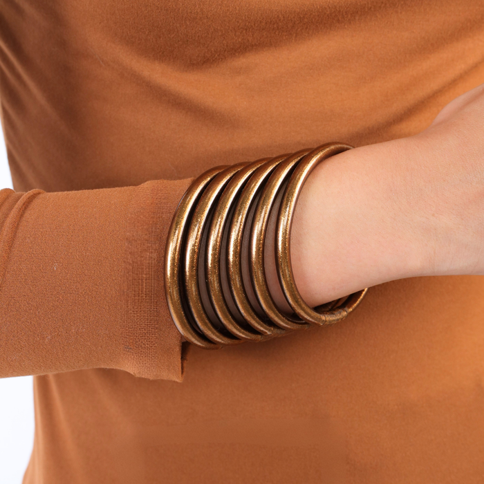 A stack of bronze bangle bracelets worn on a person's wrist, shown against a matching rust-brown long-sleeve top.