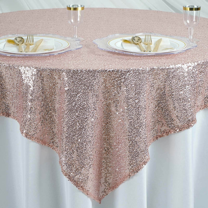 Rose gold sequin tablecloth draped over a round table with plates and utensils. #whtbkgd