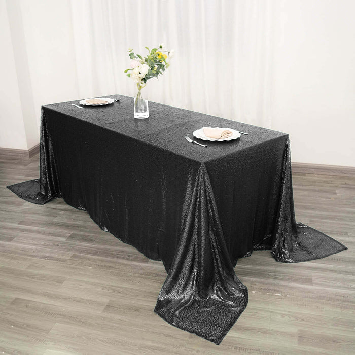 Black sequin tablecloth draped elegantly over a dining table with plates and flowers.