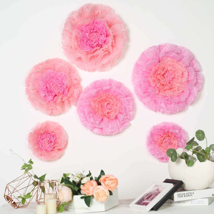 Pink tissue paper flowers arranged on a wall with decorative plants and vases.