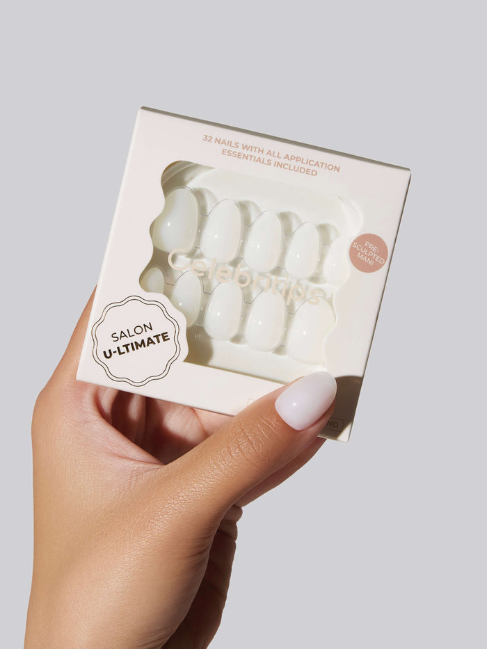 A hand with white nails holding a box of white Salon U-ltimate white press-on nails.
