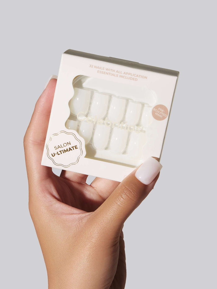 Hand with white coffin press-on nails holding a package of the nails.