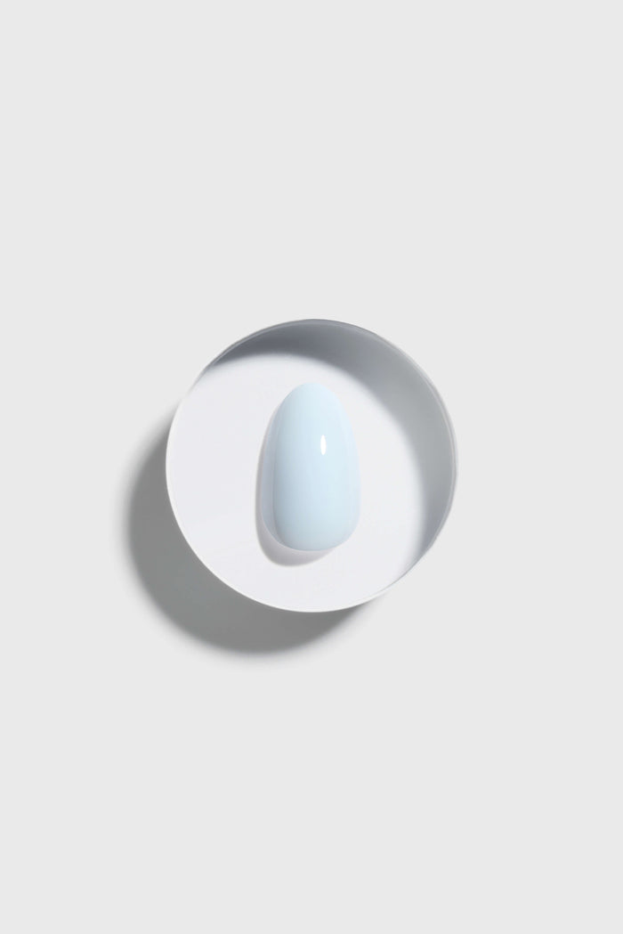sky blue press-on nail on a white surface with a gray circular shadow