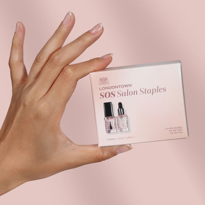 A perfectly manicured hand holds a box labeled "S.O.S. Salon Staples" from LONDONTOWN, containing two nail product bottles—your secret to flawless nails—set against a pink background.