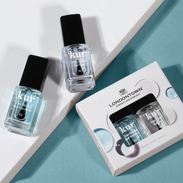 Three LONDONTOWN kur nail care products, featuring a nail strengthener and the boxed Strength & Shine Duo, are displayed on a blue and white surface.