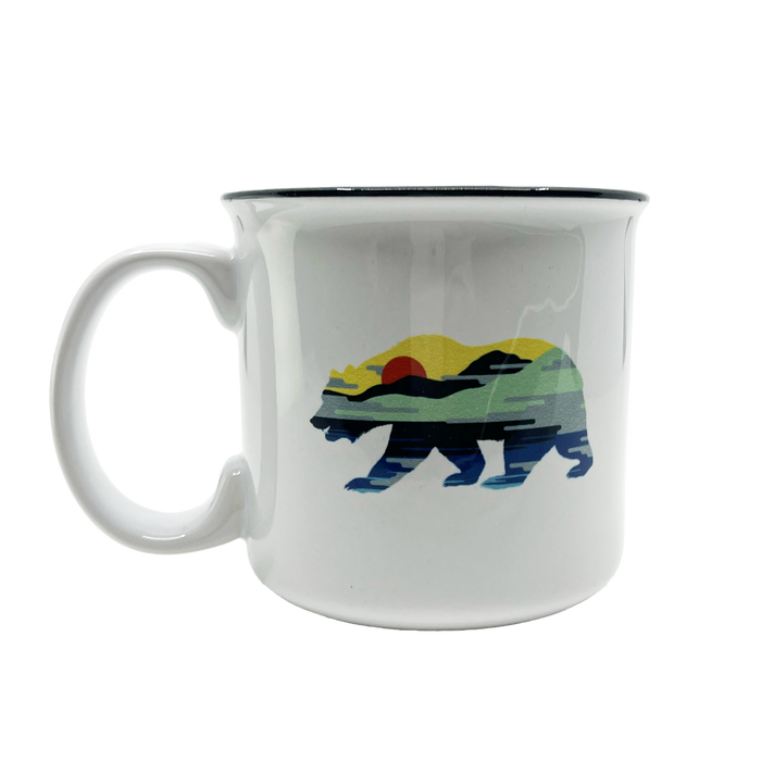 Introducing the Sunset Bear Coffee Mug by Oaklandish, a white ceramic mug adorned with a vibrant California grizzly design. The bear is filled with a captivating landscape scene featuring a red sun, green and yellow hills, and a blue sky. It is elegantly accented with a black rim and sturdy handle against its plain white background.