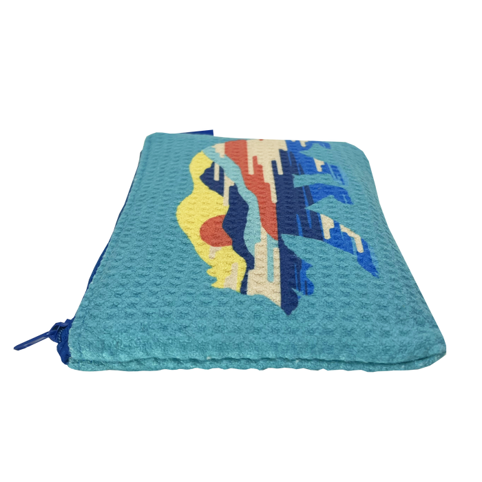 The Sunset Bear Pouch by Oaklandish is displayed horizontally. It has a textured waffle weave and comes in light blue with a vibrant, abstract design on the front, featuring a red sun setting over blue and yellow mountains. The zip pouch features a zipper closure along the side in matching blue color.