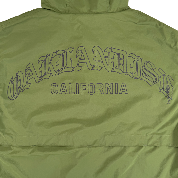 The Susurrus Track Top by Oaklandish is a light green nylon men's jacket with a hood, featuring bold “OAKLANDISH” lettering in black across the back and “CALIFORNIA” below. It sports classic fit, visible stitching, and a slight sheen for extra style.