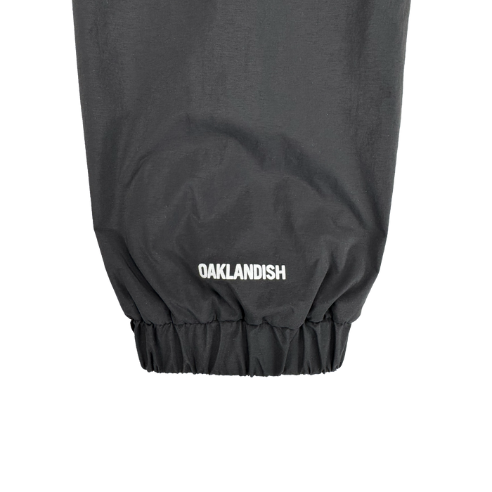 Close-up of the Susurrus Track Top's black sleeve with an elastic cuff. "Oaklandish" is boldly printed in white near the cuff, highlighting the brand on this men's zip jacket.