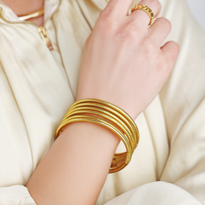 Gold bangles on a hand with a white fabric blouse.