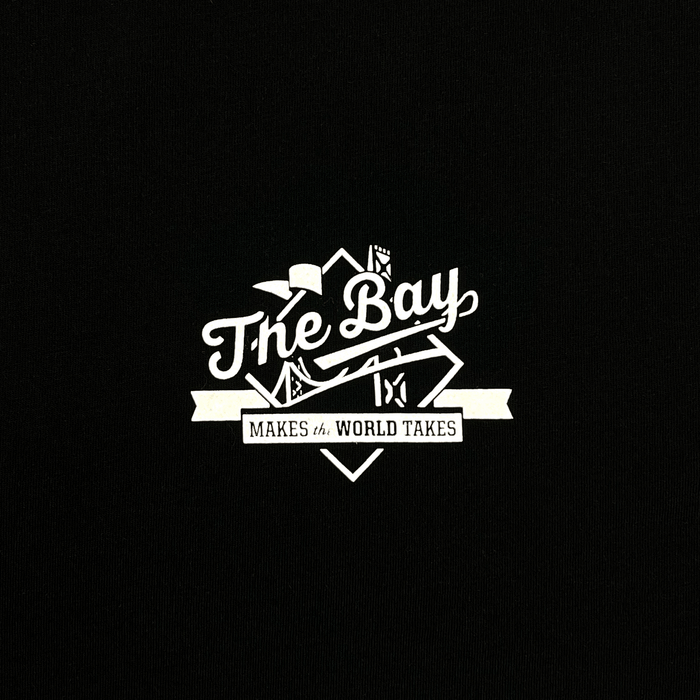 A crisp white graphic on a black background spells out “The Bay” in flowing cursive, topped with stylized illustrations of a bridge and cityscape in homage to Bay Area culture. Beneath, a bold banner proclaims “MAKES th WORLD TAKES” in all caps. This minimalist motif is printed on the classic fit The Bay Tee by DOC, part of Other’s signature Bay Collection.