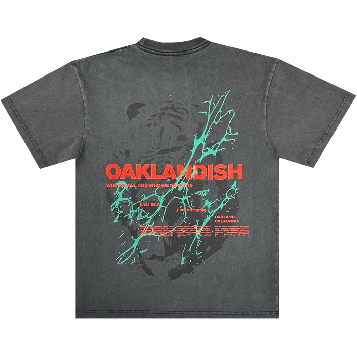 The Oaklandish Tiger Blood Tee is a vintage black 100% cotton shirt with bold red “OAKLANDISH” text across the back, a stylized black bear, teal paint splatters, and smaller white and red dates plus “Oakland, California” below.
