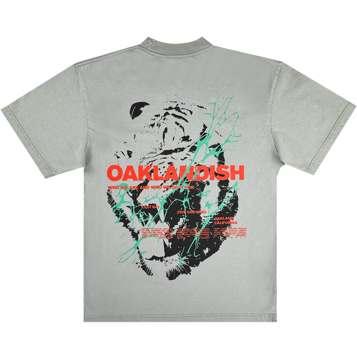 The Tiger Blood Tee by Oaklandish is a vintage grey heavyweight cotton shirt featuring a bold black and white tiger face graphic on the back, with striking red "OAKLANDISH" text, white and red details, and green accent lines.