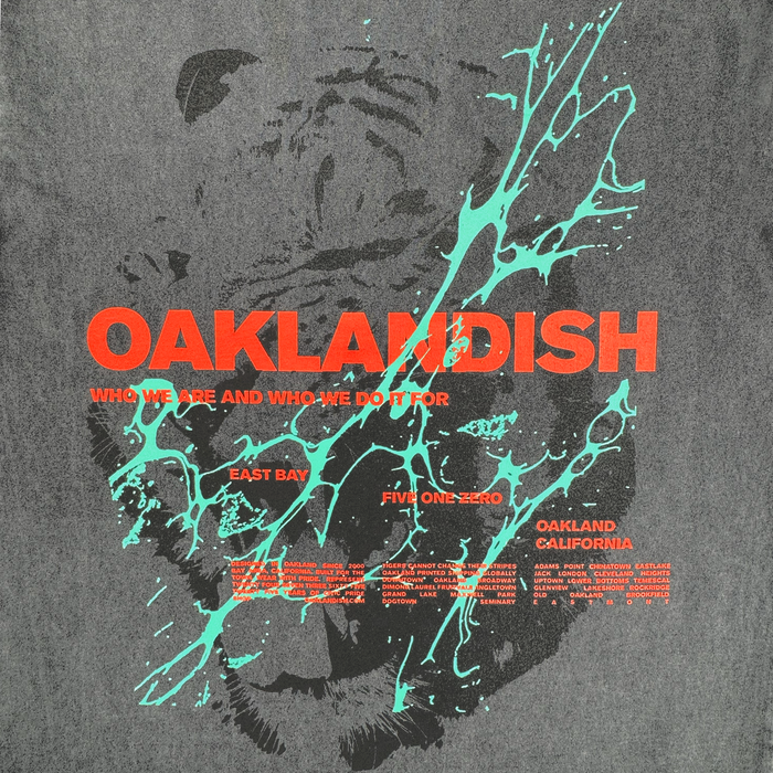 The Tiger Blood Tee by Oaklandish features bold orange-red "OAKLANDISH" text over a grayscale tiger face on a vintage black shirt with turquoise splatters, plus phrases like "Who we are and who we do it for," "East Bay," and "Oakland California.