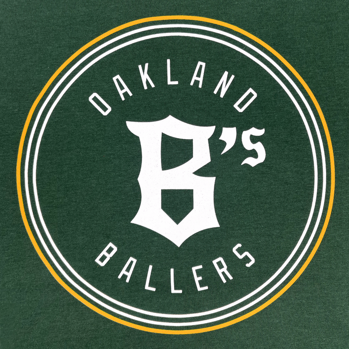 A green background showcases the Oakland Ballers logo with a distinctive circular design in white and yellow. At the center of the circle, "OAKLAND BALLERS" is emphasized in uppercase white letters. Prominently positioned in the middle is a large white stylized "B", accompanied by a small "'s" on its upper right side, symbolizing Oakland's professional baseball team in the Pioneer League, as featured on the Toddler Oakland Ballers Logo Tee from Oakland Ballers.