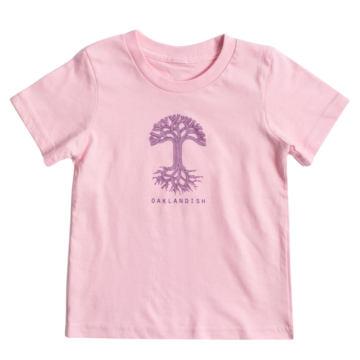 A light pink, 100% cotton Toddler Oaklandish Classic Logo Tee from Oaklandish featuring a purple tree graphic with intricate branches and roots in the center. Below the tree, "OAKLANDISH" is printed in a simple, all-caps font. The t-shirt is laid flat against a white background.