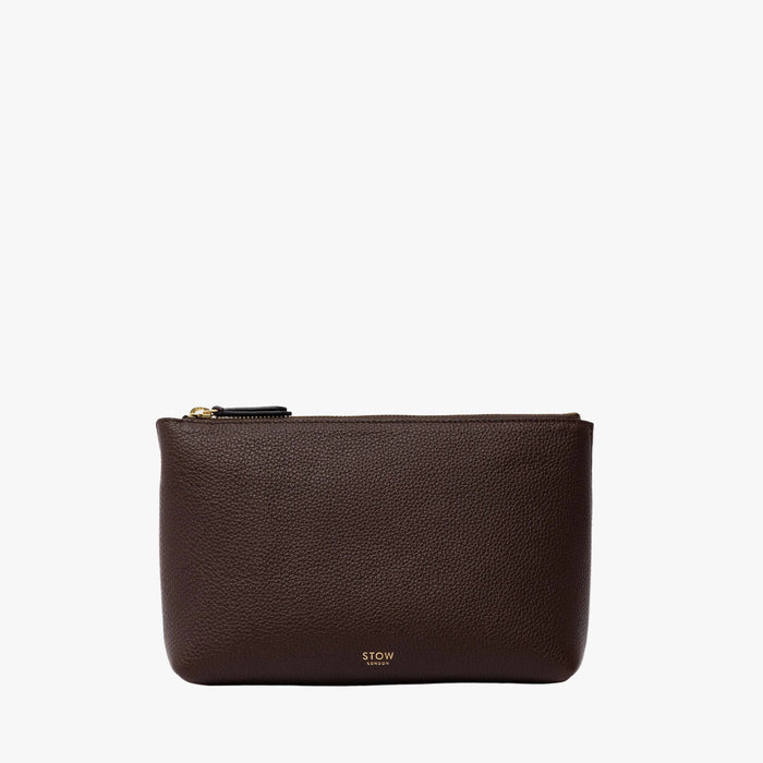 STOW London's travel pouch in Espresso pebbled leather on a light grey background featuring a YKK zip and a fine gold embossed logo on the front