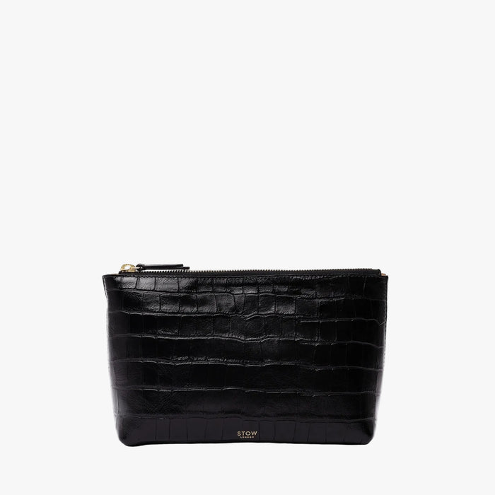 STOW London's travel pouch in Black Embossed Croc leather on a light grey background featuring a YKK zip and a fine gold embossed logo on the front