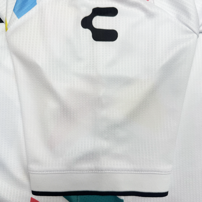 Close-up of an Oakland Roots SC Unisex Mosaic in Motion Kit sleeve: features a white mosaic texture, thin dark hem stripe, black abstract symbol by the shoulder, and colorful blue, yellow, and red geometric shapes in the background.