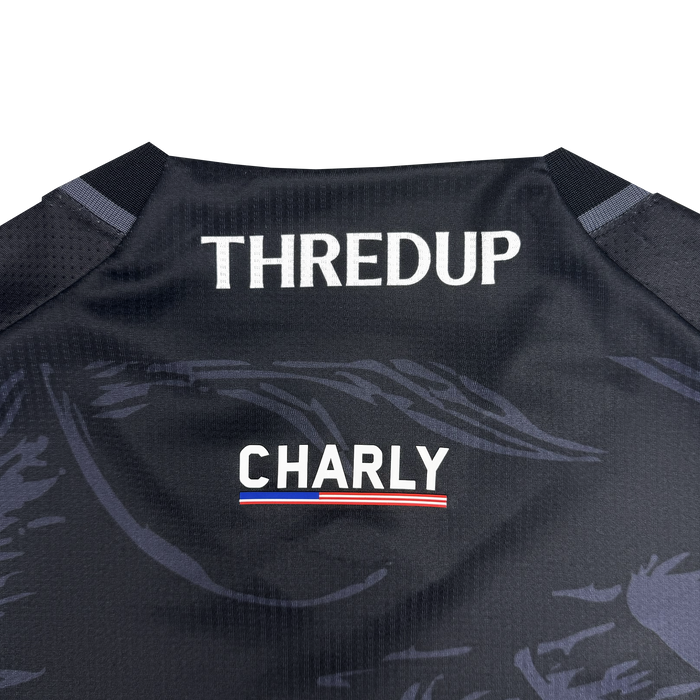 Close-up of the Unisex Oak-ness Awakens Kit by Oakland Roots SC—a black jersey with “THREDUP” in bold white, “CHARLY” below, and a red, white, and blue stripe—featuring subtle patterns inspired by the legendary Oak-ness Monster.