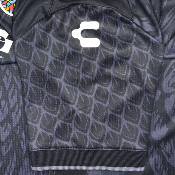 Close-up of the Oakland Roots SC Unisex Oak-ness Awakens Kit—a black sports jersey with a subtle geometric pattern, white “C” logo, and multicolored patch nodding to the Oak-ness Monster legend of Lake Merritt.