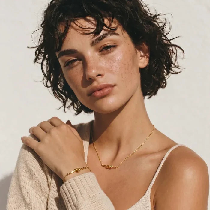 Unity Knot Necklace in gold-tone metal with a fine chain and small horizontal knot pendant, paired with a matching bracelet