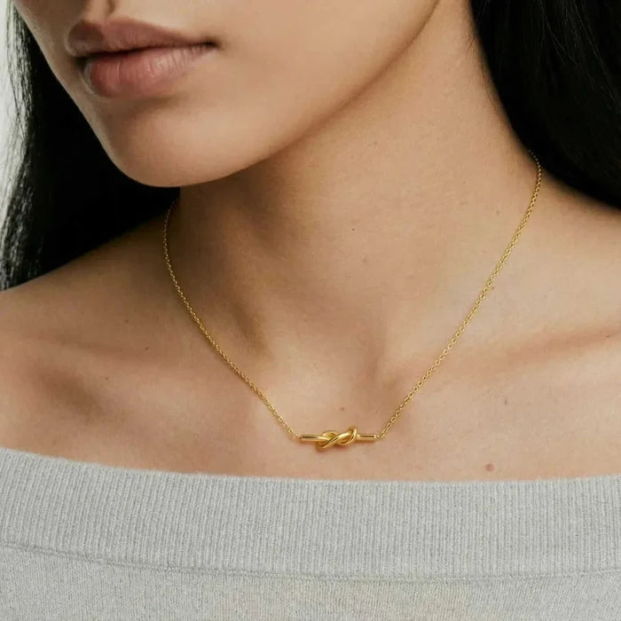 Unity Knot Necklace in polished gold-tone metal, featuring a fine chain and small horizontal looping knot pendant