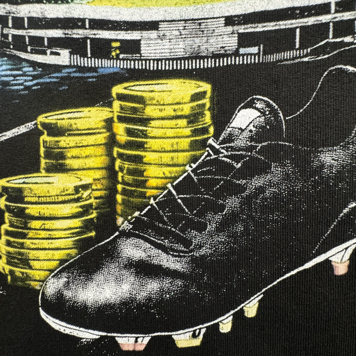 A close-up of the Oakland Roots SC Wager Tee set before stacks of gold coins with a stadium backdrop, highlighting the link between sports and money for the club.