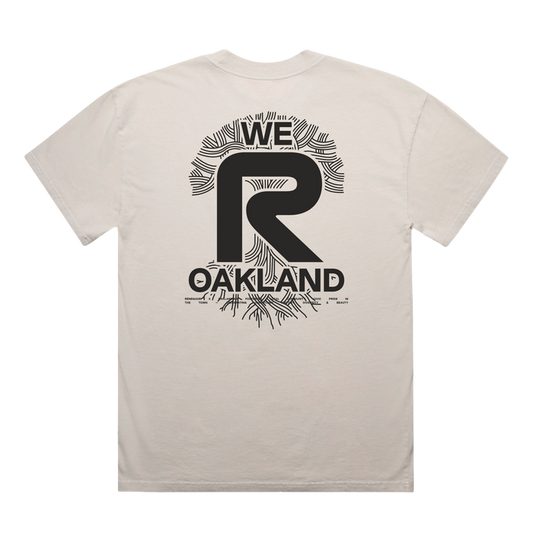 Back of the Oaklandish We R Oakland Tee in light beige, heavy-weight cotton, features a bold black graphic: a large central "R" with "WE" above and "OAKLAND" below, all encircled by abstract palm-like radiating lines.