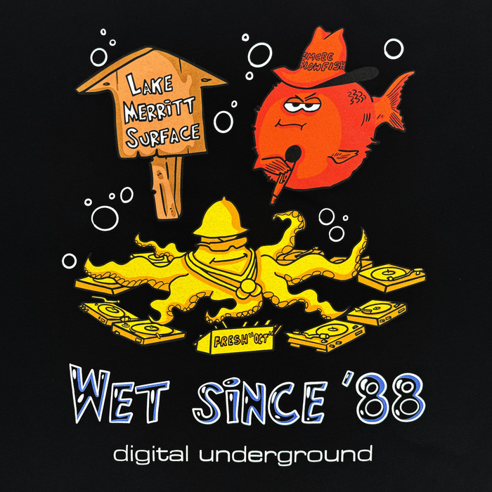 A cartoon octopus DJ spins records underwater beside a “Lake Merritt Surface” sign, channeling classic Oakland t-shirt vibes on the Wet Since ’88 Tee by Other. A red fish in sunglasses smokes and blows bubbles reading “Peace Munki!” while bold white text below states “WET SINCE ‘88” and “digital underground Underwater Rimes.”.