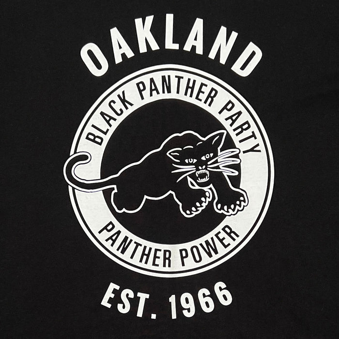 The Women's Black Panther Power Tee by Oaklandish features a circular logo with a poised black panther, accompanied by the words "Black Panther Power." The word "Oakland" is above the circle and "Est. 1966" below, all set against a striking black background with white text and imagery that pays homage to one of the era's most impactful community organizations.