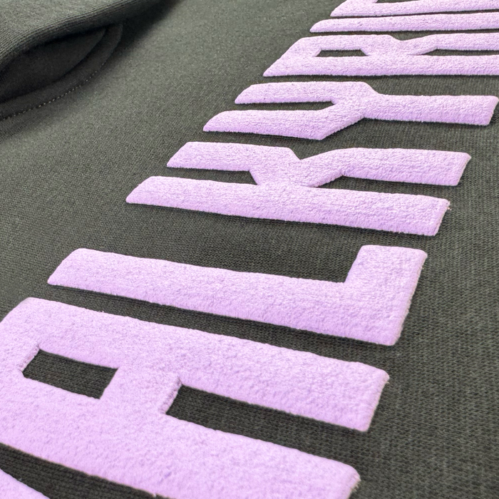 Close-up of the Women's Golden State Valkyries Violet Lightning Hoodie by GSV, showing bold, raised light purple "Golden State Valkyries" letters with a velvety texture contrasting against the smooth black fabric. Some lettering is partially out of frame.