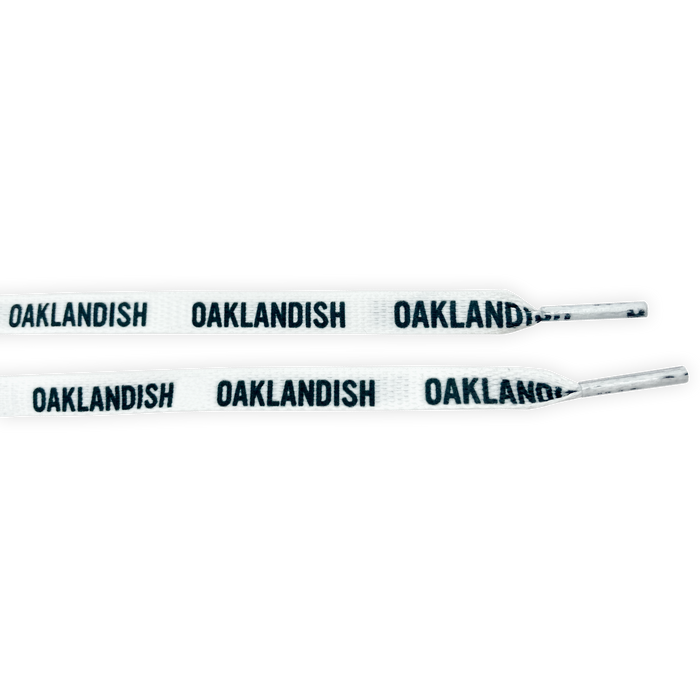 The Wordmark Shoelaces by Oaklandish are made of polyester and come in white with black "OAKLANDISH" text repeated along their length. The ends, or aglets, are also white. These flat shoelaces are neatly displayed parallel to each other against a plain background.