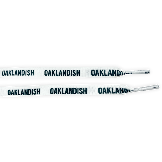The Wordmark Shoelaces by Oaklandish are made of polyester and come in white with black "OAKLANDISH" text repeated along their length. The ends, or aglets, are also white. These flat shoelaces are neatly displayed parallel to each other against a plain background.