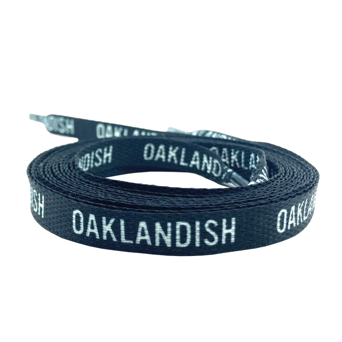 The Wordmark Shoelaces by Oaklandish, made from 100% polyester and featuring a woven texture, are displayed coiled against a white background. These flat black shoelaces have the text "OAKLANDISH" repeatedly printed in white and include standard tipped ends.