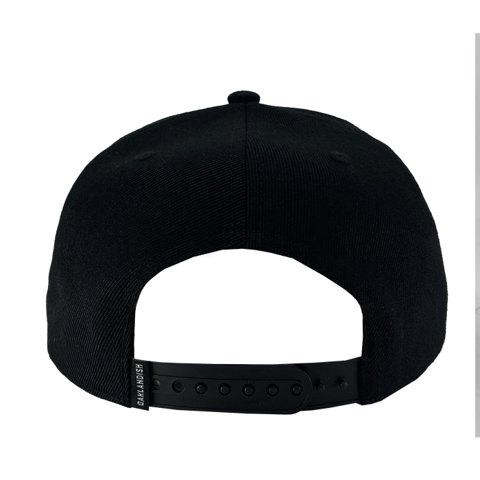 A rear view of the WPBA Snapback baseball cap by Oaklandish showcases its adjustable snapback closure with a combination of small and large holes for size customization. A small tag reading "GRANDMSH," which supports the empowerment of women in sports, is attached to the left side. The cap is black and plain, free from any additional designs.