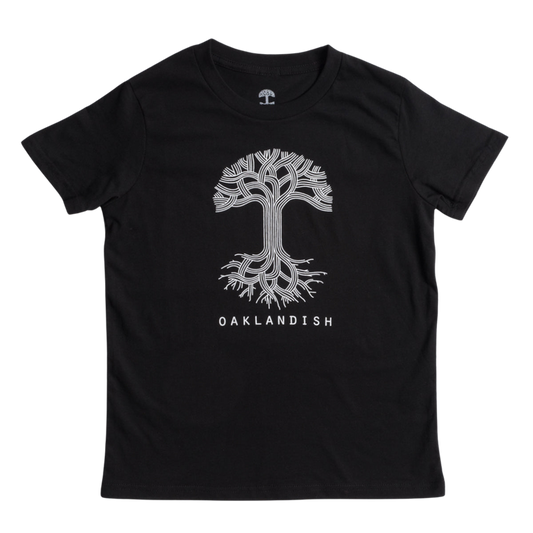 The image shows the Youth Oaklandish Classic Logo Tee by Oaklandish, a black tee made from 100% cotton. It features a white graphic of a tree with branches extending upward and roots spreading downward. Below the tree graphic, "OAKLANDISH" is written in white capital letters. The kids' t-shirt is laid flat against a white background.
